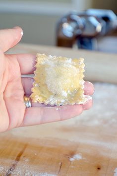 a hand holding a small piece of food on top of a wooden table