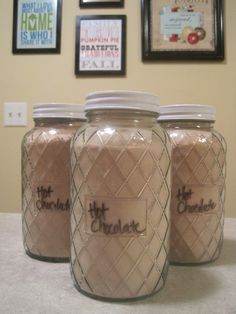 three jars with the words hot chocolate on them are lined up in front of some pictures