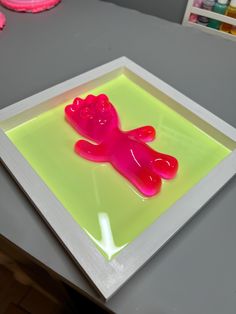 a pink teddy bear is on a green and yellow square with some paint in the background