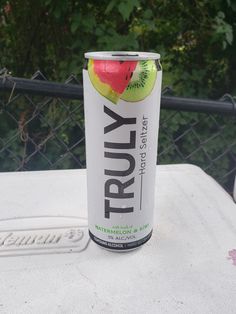 a can of fruity soda sitting on top of a white table next to a chain link fence