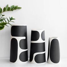 three black and white vases sitting on top of a table next to a plant