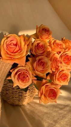 a basket filled with lots of orange roses on top of a white tablecloth covered bed