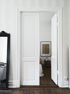 an open door leading to a bedroom with white walls and wood floors in the room