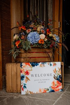 a welcome sign sitting on top of a wooden crate filled with flowers and greenery