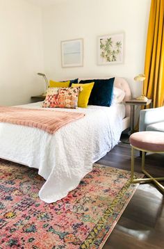 a white bed with colorful pillows on top of it and a rug in front of it