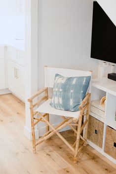 a wooden chair with a blue pillow on it in front of a flat screen tv