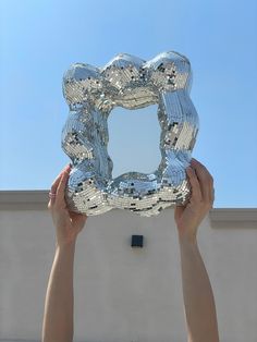 two hands holding up a large mirror in front of a building with a sky background