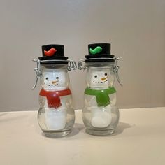 two snowmen in hats and scarfs are sitting inside glass jars with magnets on the lids