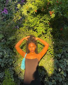 a woman is standing in the middle of some bushes and trees with her hands on her head