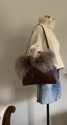 "This large structured shoulder bag measures 16 1/2\"w x 10 1/2\"h and has a shearling detail across the top on the front of the bag. There is one interior cell phone pocket and a wrap closure that loops around a sustainably gathered, naturally shed deer antler. The handle is 29\" long." Luxury Shoulder Bag With Faux Fur Lining, Elegant Rectangular Shoulder Bag With Faux Fur Lining, Winter Leather Tote Bag, Luxury Sheepskin Bags With Faux Fur Lining, Leather Bag With Faux Fur Lining, Rectangular Travel Shoulder Bag With Faux Fur Lining, Leather Shoulder Bag For Winter, Winter Leather Shoulder Bag, Luxury Leather Shoulder Bag With Faux Fur Lining