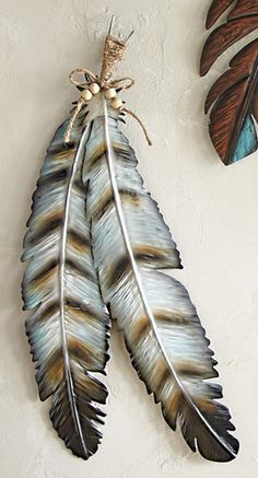 two metal feathers hang on the wall next to each other, one is brown and blue