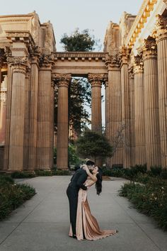 a man and woman kissing in front of an old building with columns on either side