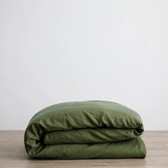 two green pillows sitting on top of each other in front of a white wall and wooden floor