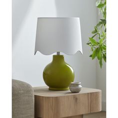 a green vase with a white shade on it sitting on a table next to a lamp