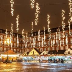 people are walking around in front of some buildings with christmas lights hanging from the ceiling