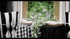 the table is set with black and white linens, silverware and greenery