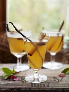 two glasses filled with drinks sitting on top of a wooden table next to leaves and flowers