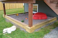 a dog laying on the ground in front of a wooden structure with sand and toys