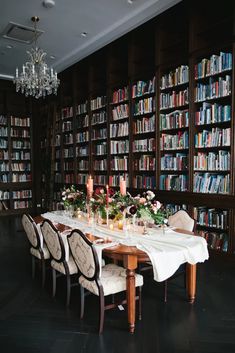 a dining room table is set with candles and flowers in front of bookshelves