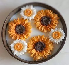 six sunflowers are placed in a bowl on a table top with white and yellow flowers