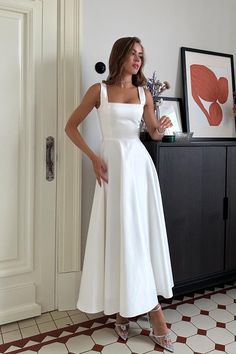 a woman in a white dress standing next to a cabinet