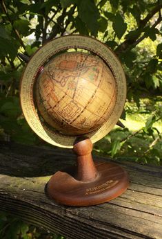 an old wooden globe sitting on top of a tree branch in the sun with green leaves behind it