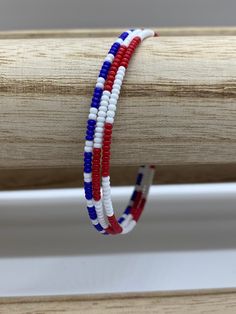 red, white and blue beaded bracelets sitting on top of a piece of wood