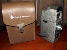 two old fashioned cameras sitting next to each other on a wooden floor in front of a wall