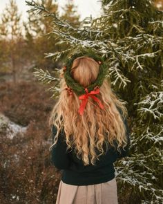 a woman with long blonde hair wearing a wreath on her head and standing in front of a tree