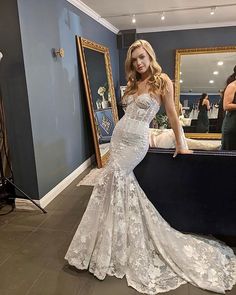 a woman standing in front of a mirror wearing a wedding dress