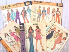 four vintage sewing patterns for women's tops and pants on a white wooden surface