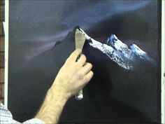 a man is painting a mountain scene on a black board with white paint and silver foil