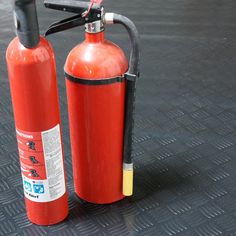 two red fire extinguishers sitting on top of a black floor next to each other