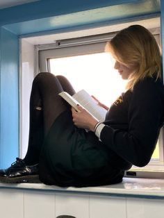 a woman sitting on a window sill reading a book