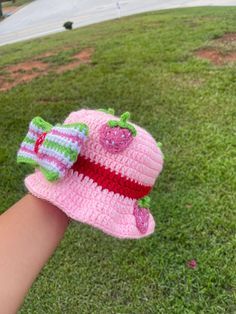 a hand holding a pink crocheted hat on top of green grass