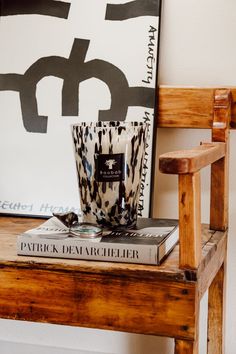 a wooden chair sitting next to a table with a book on it and a candle