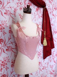 A pair of Balletcore Renaissance, Baroque, Rococo, Regency, Victorian Era Corset Stays in Ballet Pastel Pink with Rosette Appliques in front of a toile backdrop. Corset Stays, Baroque Era, Delicate Dress, Fantasy Shop, Tudor Era, Puffy Skirt, Pink Corset, Ballet Pink, Medieval Fashion