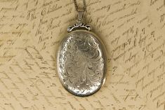 This large locket features a detailed engraving of scrolling vines and a flower on the front. The back is plain. The bail attaches to a lovely scrollwork piece at the top of the locket, adding charming detail to this already beautiful piece. The locket hangs on a beautiful vintage sterling box chain that closes with a spring ring clasp. Both original inserts are included. The locket is marked "sterling" on the back near the bottom, preceded by an "E" in a diamond and followed by a tiny, stylized Ornate Engraved Antique Silver Locket Necklace, Vintage Antique Silver Locket Necklace For Anniversary, Antique Silver Vintage Locket Necklace For Anniversary, Vintage Etched Locket Necklace For Anniversary, Vintage Engraved Antique Silver Jewelry, Antique Silver Engraved Locket Necklace For Anniversary, Ornate Engraved Locket Necklace For Formal Occasions, Ornate Engraved Locket Necklace For Formal Events, Ornate Locket Necklace For Formal Occasions