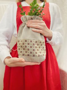 a woman in red dress holding a small bag with plants inside and green leaves on it