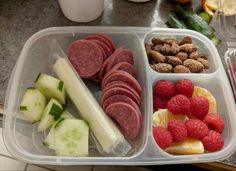 a plastic container filled with meat, fruit and veggies on top of a table