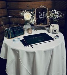 a table topped with a notebook and camera next to a vase filled with white flowers