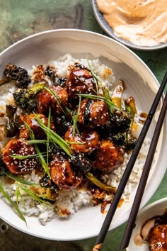 a white bowl filled with meat and vegetables on top of rice next to chopsticks