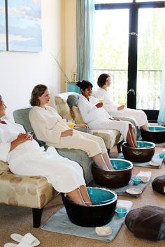 four women in robes are sitting on couches and having drinks at the same time