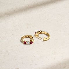 Two vibrant rubies rest alongside a sparkling petite diamond in this minimalist and timeless style that can be worn effortlessly for a variety of occasions. Their lightweight nature makes them a comfortable essential that is suitable for styling solo or stacked with other similar huggies. Metal: 18kt Gold Ruby Weight: 0.40 ct. Diamond Weight: 0.21 ct. Measurements: 12.5 mm drop *Please note that the listed ct. weights are approximate and may be subject to slight variations. Yellow Gold Ruby Earrings With Brilliant Cut, Yellow Gold Diamond Earrings With Birthstone, Elegant Ruby Hoop Earrings For Anniversary, Elegant Round Huggie Earrings With Birthstone, Diamond Huggie Earrings, Red Spinel, Rubellite Tourmaline, Paraiba Tourmaline, Red Gemstones