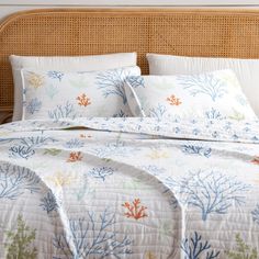 a bed with white sheets and blue corals on it's cover, in front of a wicker headboard