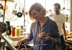 a woman is cooking in the kitchen while another man stands behind her and looks on