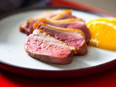 some meat and an orange on a white plate with red table cloth, ready to be eaten