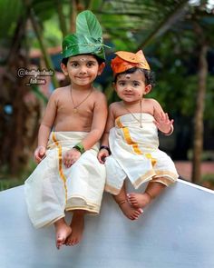 two young children sitting next to each other on top of a white bench in front of trees