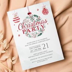 a white christmas party card on top of a bed with red and green ornaments hanging from it