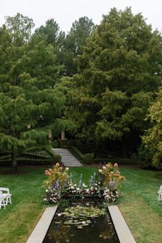 a pond with water lilies and flowers in it next to some chairs on the grass